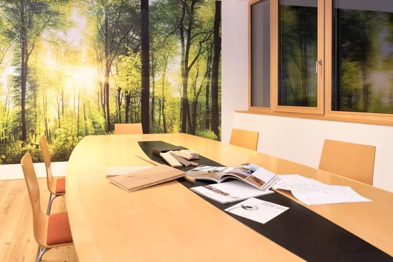 Besprechungstisch mit Mustern und Katalogen vor einer Waldtapete